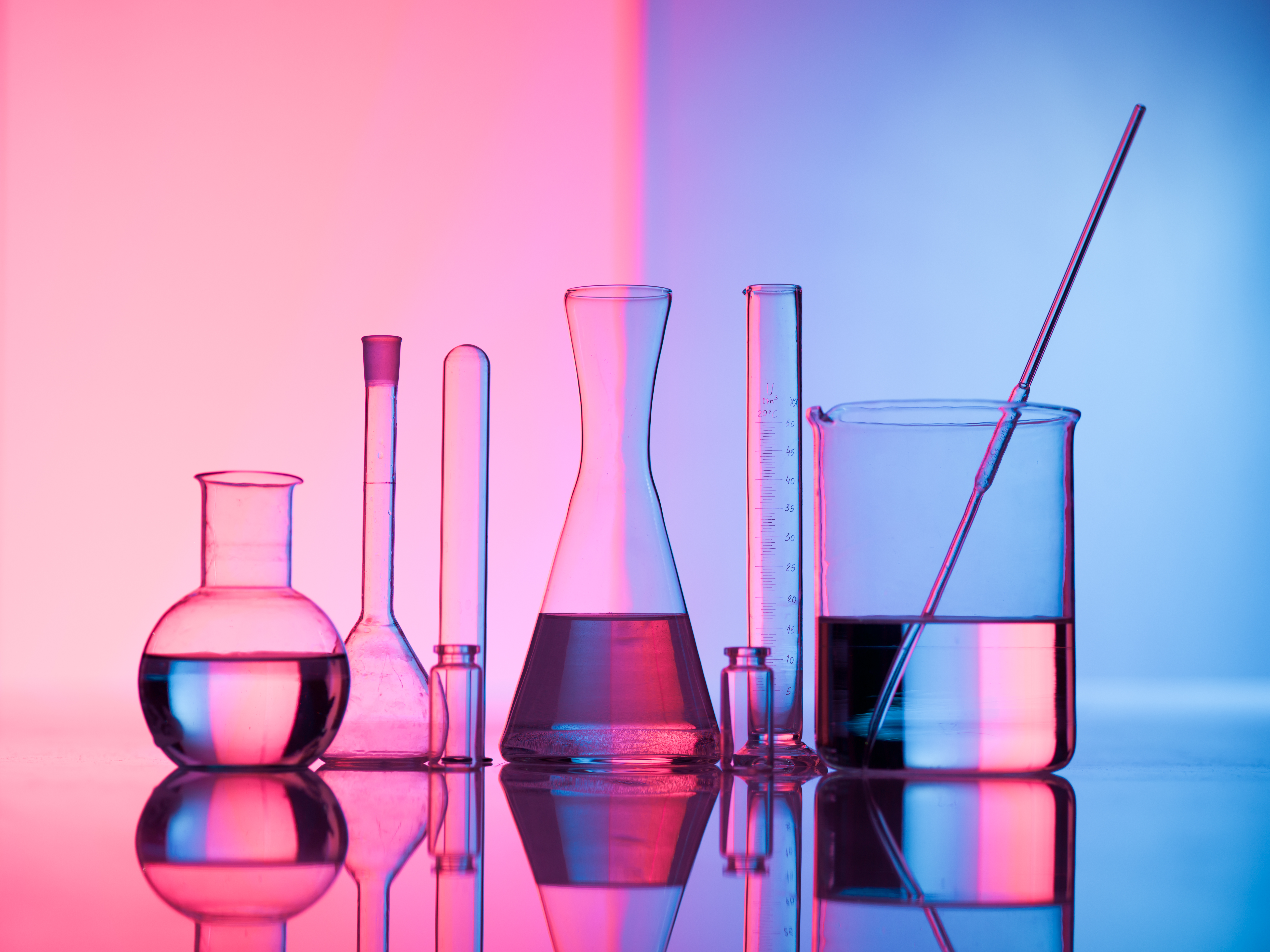 Different laboratory glassware with water and empty with reflection. Pink and blue tint background