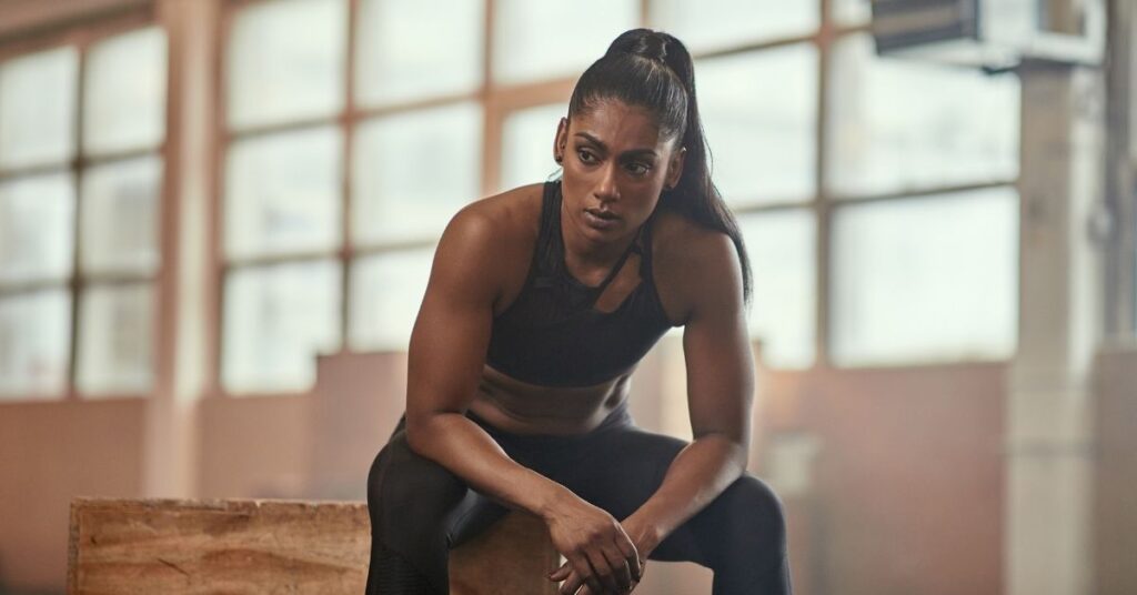 Erschöpfte Athletin pausiert nach einem intensiven Functional-Fitness-Workout zur Vorbereitung auf HYROX.